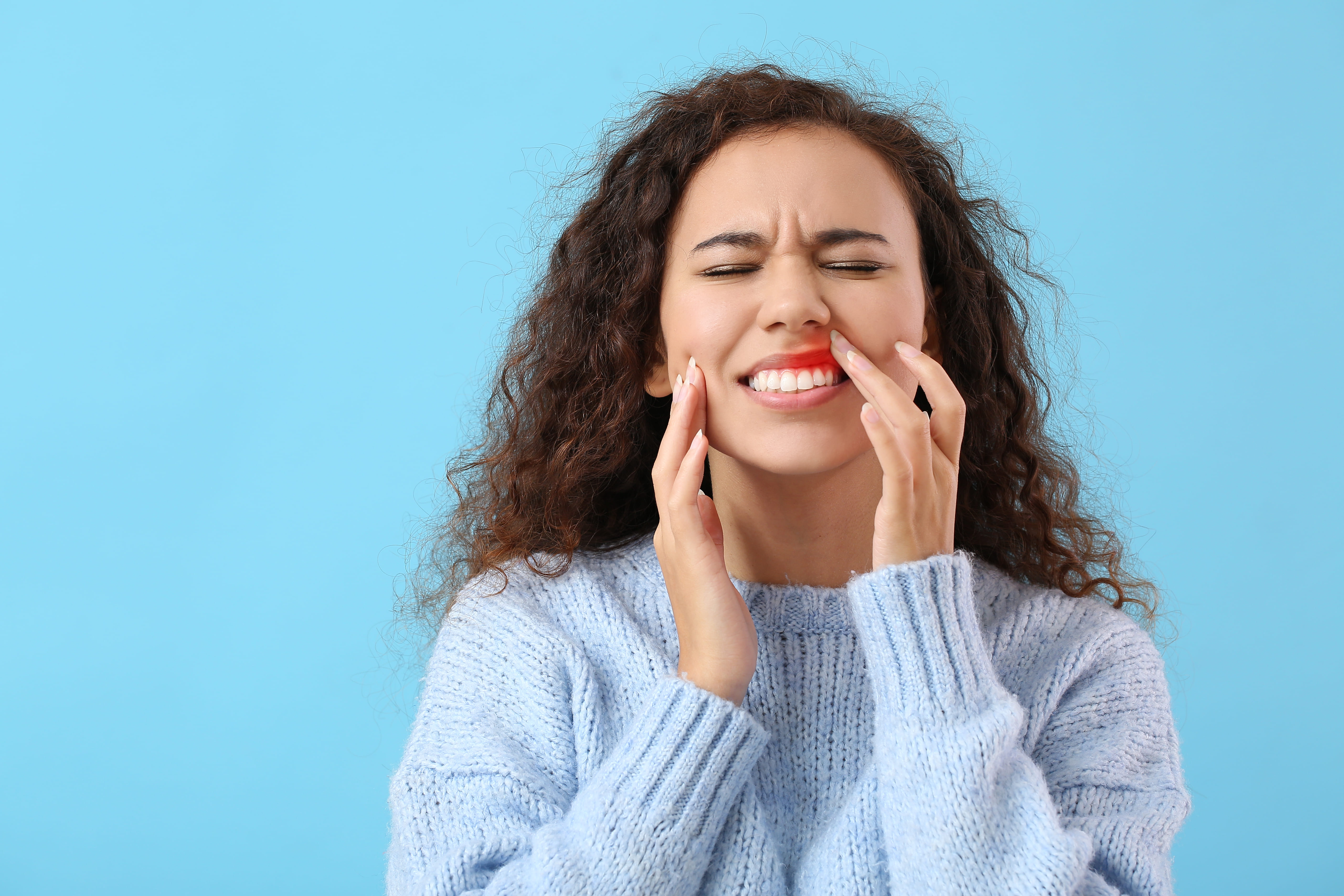 Woman with gum pain winces and gently touches her sore gums.