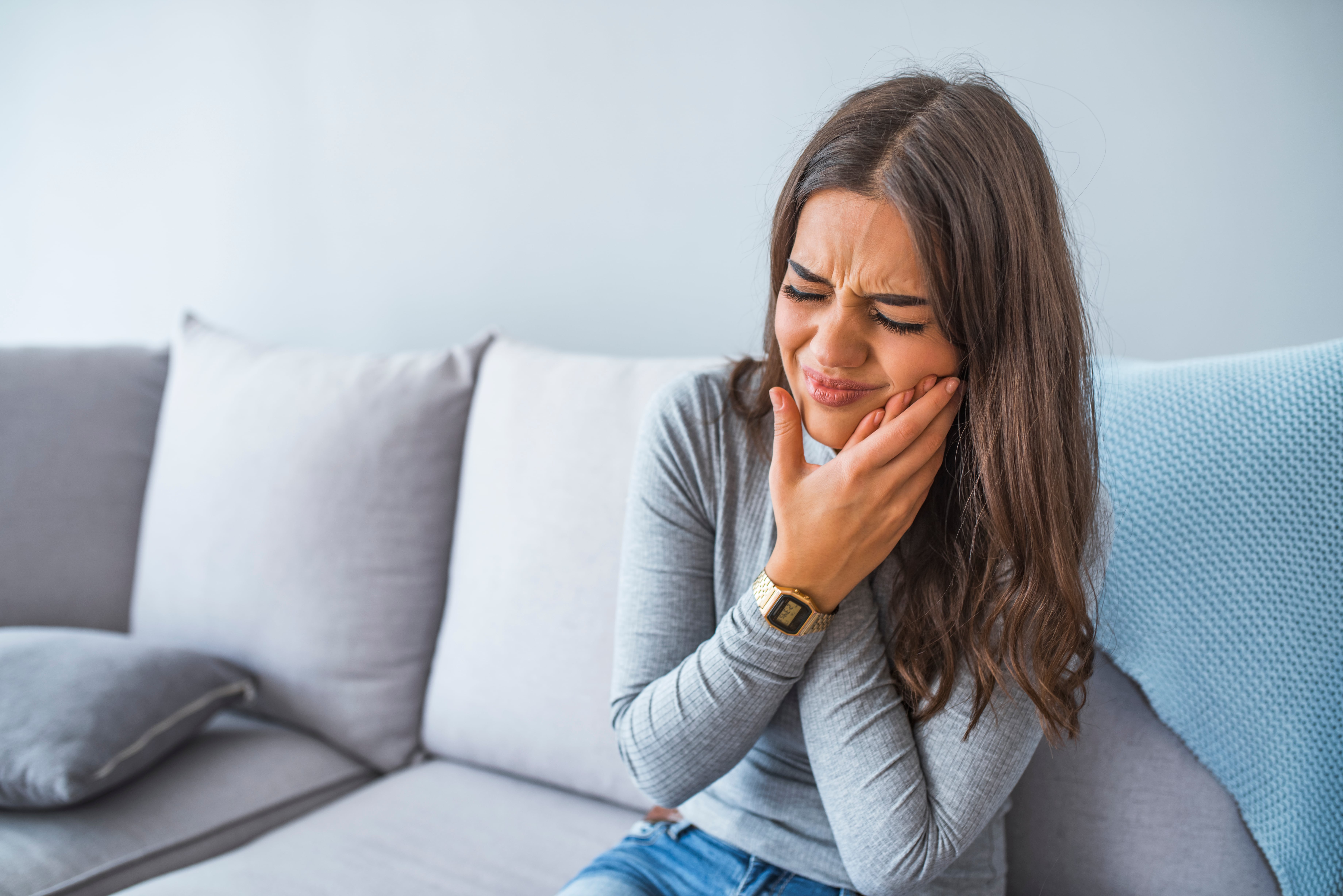 Woman holds her jaw and winces because of toothache pain.